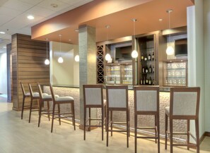 A bar area with wooden chairs, a bar counter, and shelves with bottles. - Fairfield Inn & Suites by Marriott Durham Southpoint (Durham)