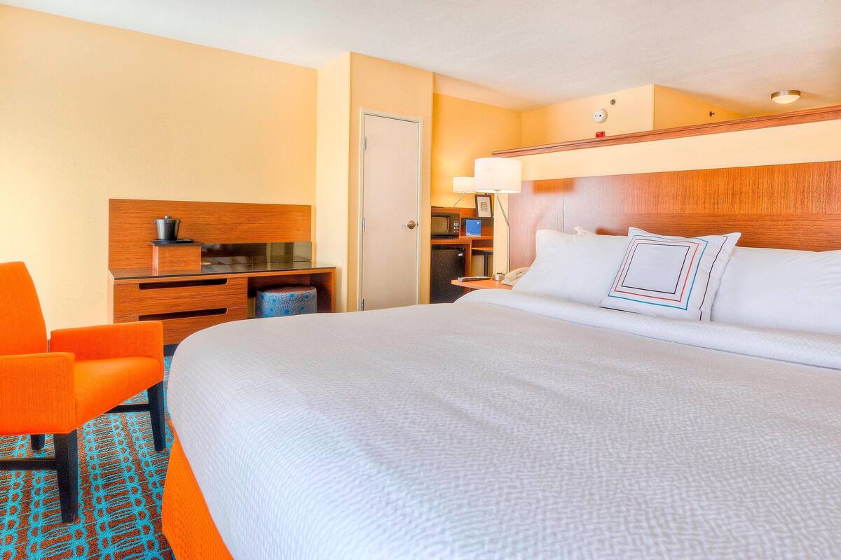 Ein Hotelzimmer mit einem großen Bett, einem Schreibtisch mit Computer, einem Stuhl und einer Mikrowelle.