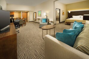 A hotel room with a bed, a sitting area with a sofa and armchairs, a dining table with chairs, a TV, and a small kitchen area. - Holiday Inn El Paso Airport by IHG (El Paso)