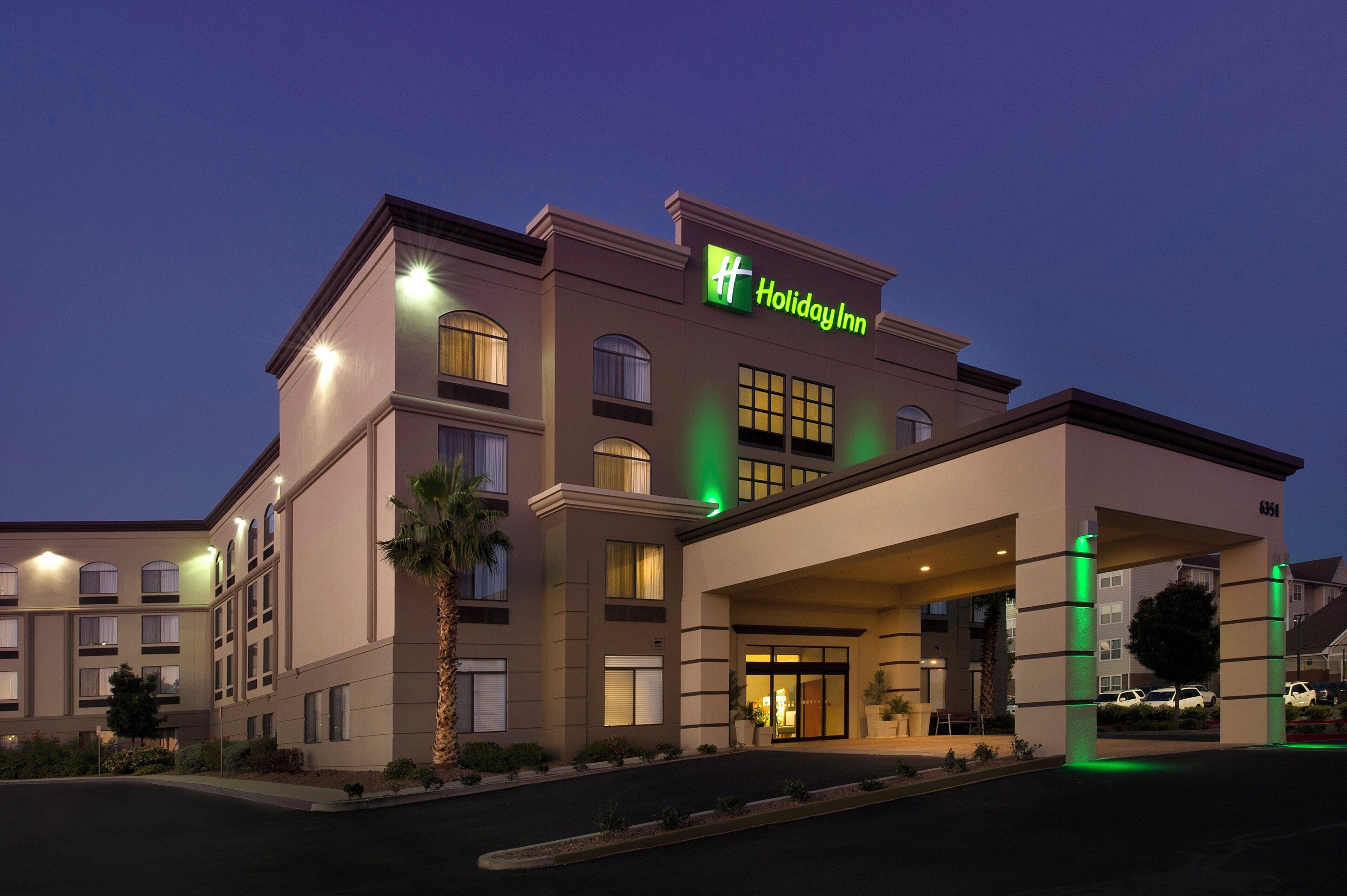 Un bâtiment d’hôtel Holiday Inn au design moderne, caractérisé par un logo vert bien visible, de nombreuses fenêtres et un espace d’entrée abrité.