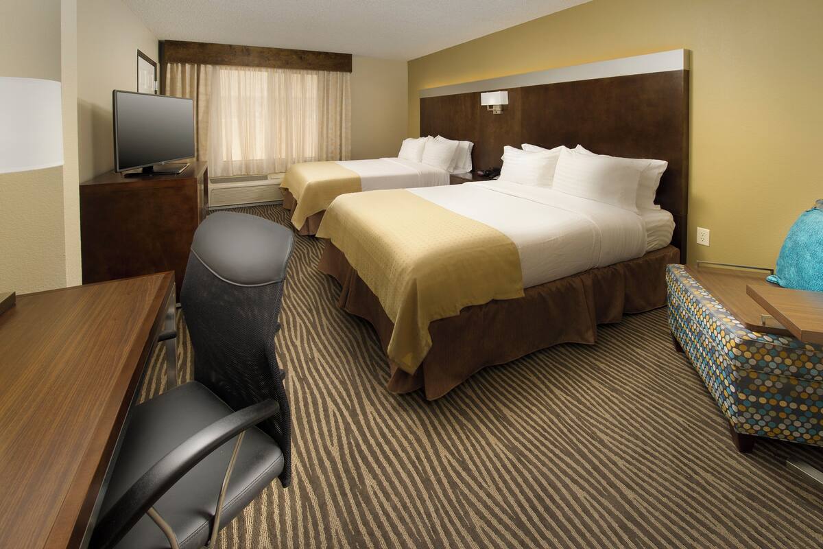 Habitación de hotel con dos camas, un escritorio con silla, televisor y alfombra estampada.