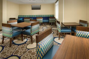 A restaurant with booths and tables, patterned carpet, and a flat-screen TV on the wall. - Holiday Inn El Paso Airport by IHG (El Paso)