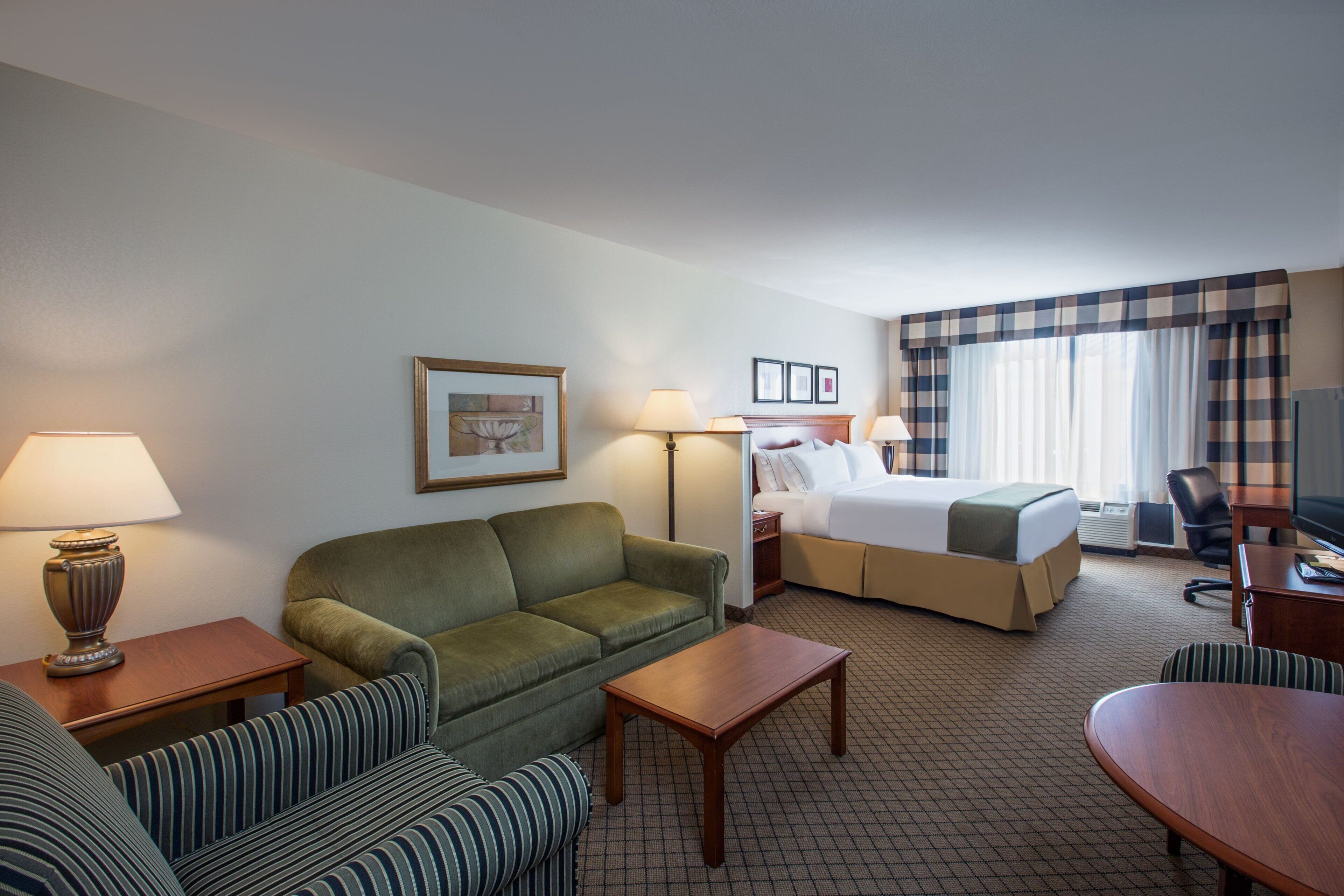 A hotel room with a bed, a sofa, a chair, a desk, and a television.