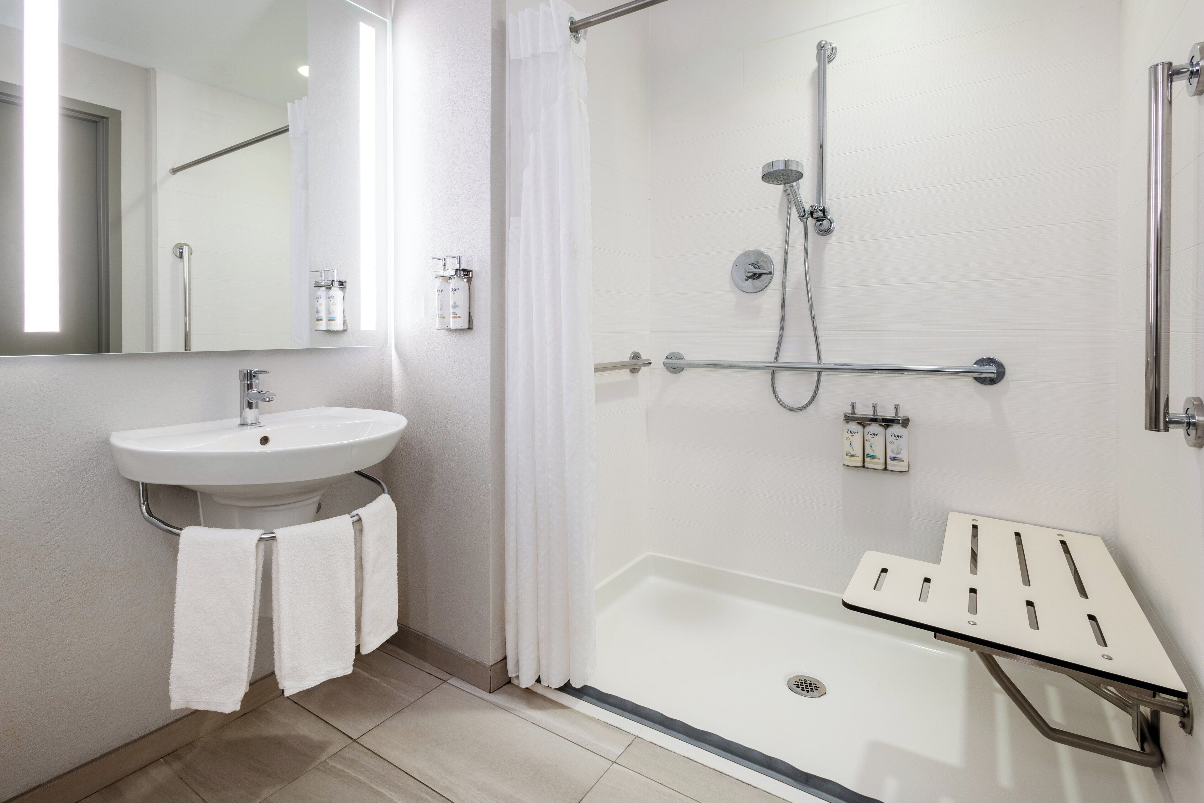 A modern bathroom with a sink, mirror, shower, and a grab bar.