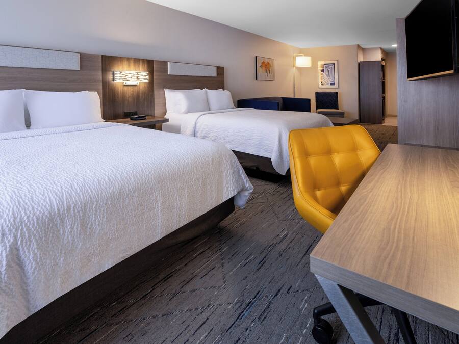 Una habitación de hotel con dos camas, una mesa de madera y una silla amarilla.