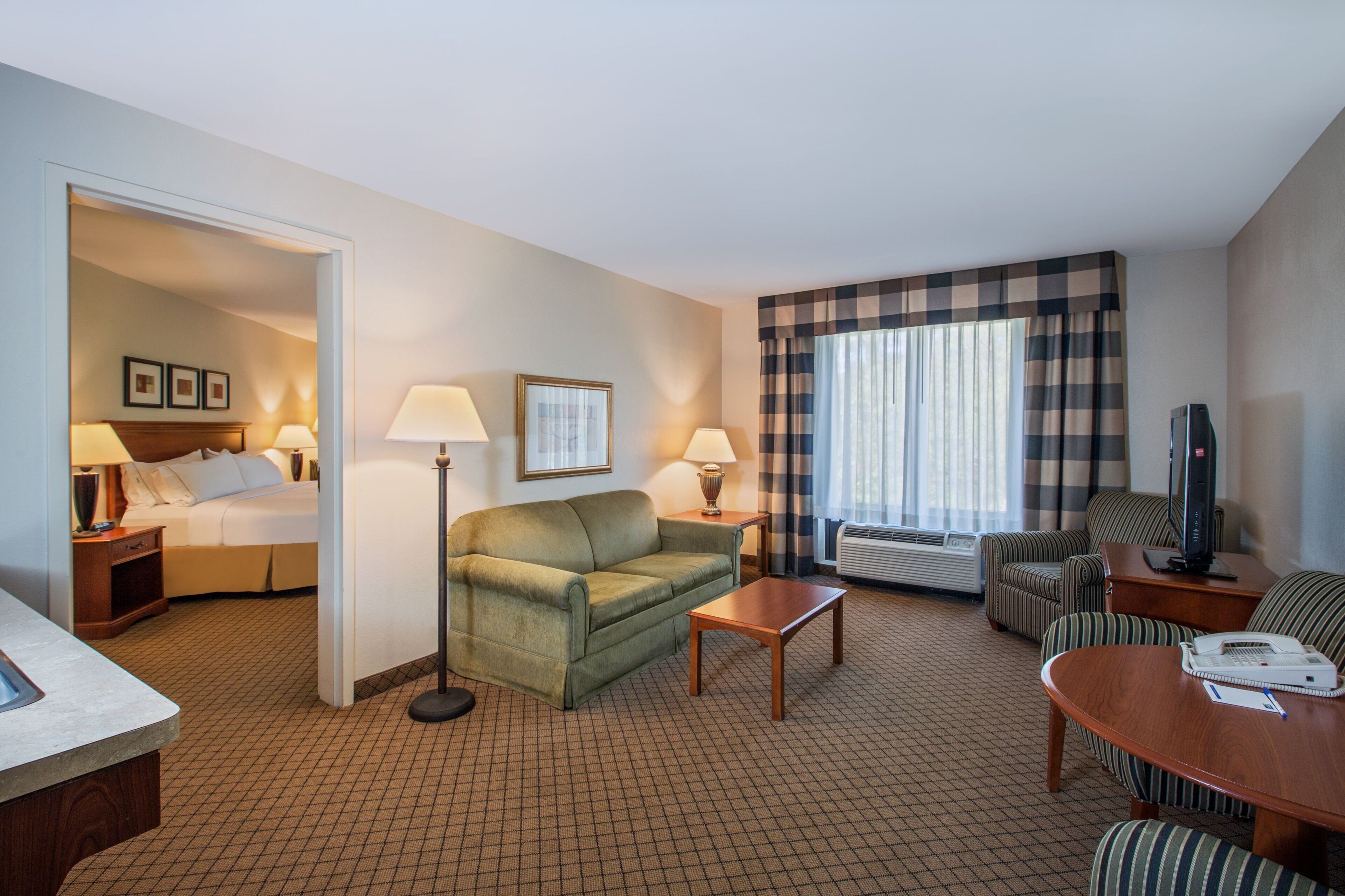 Une chambre d’hôtel comprenant un lit, un canapé, une table basse, une télévision et un bureau avec un téléphone.