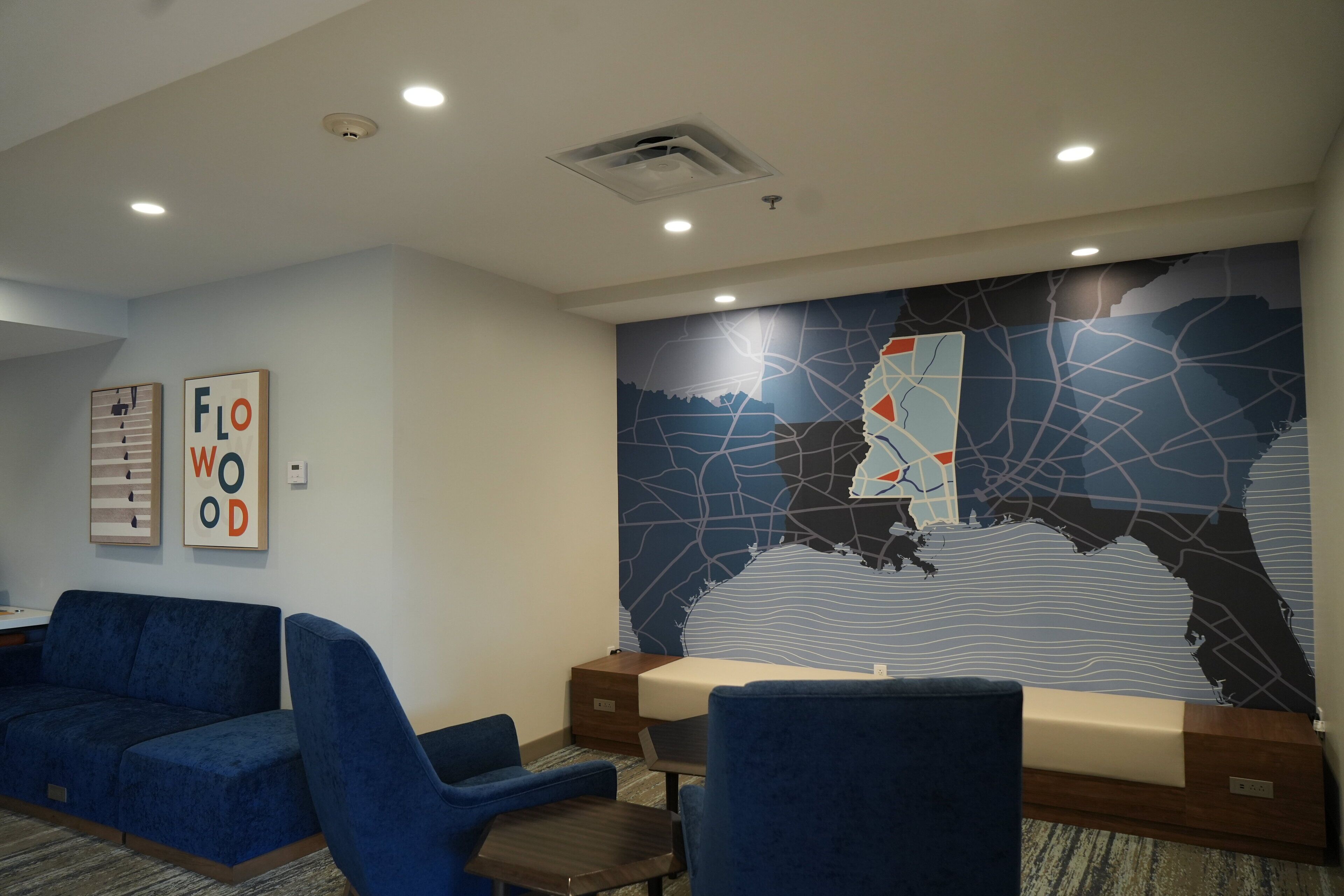 A hotel lobby with blue seating, a map mural, and a 'Flow Wood' sign.