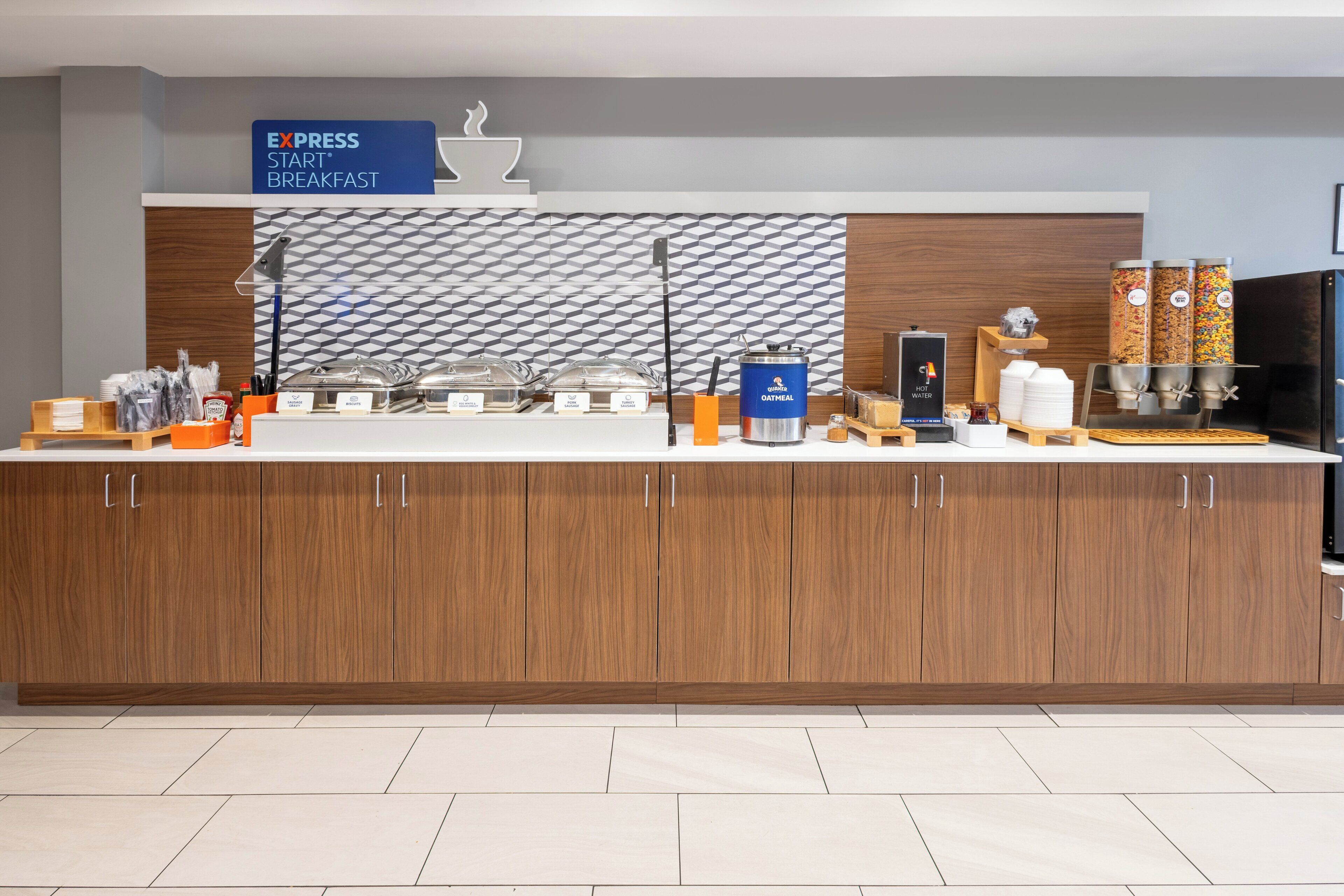 A breakfast buffet counter with labeled containers for oatmeal, hot water, and other beverages.