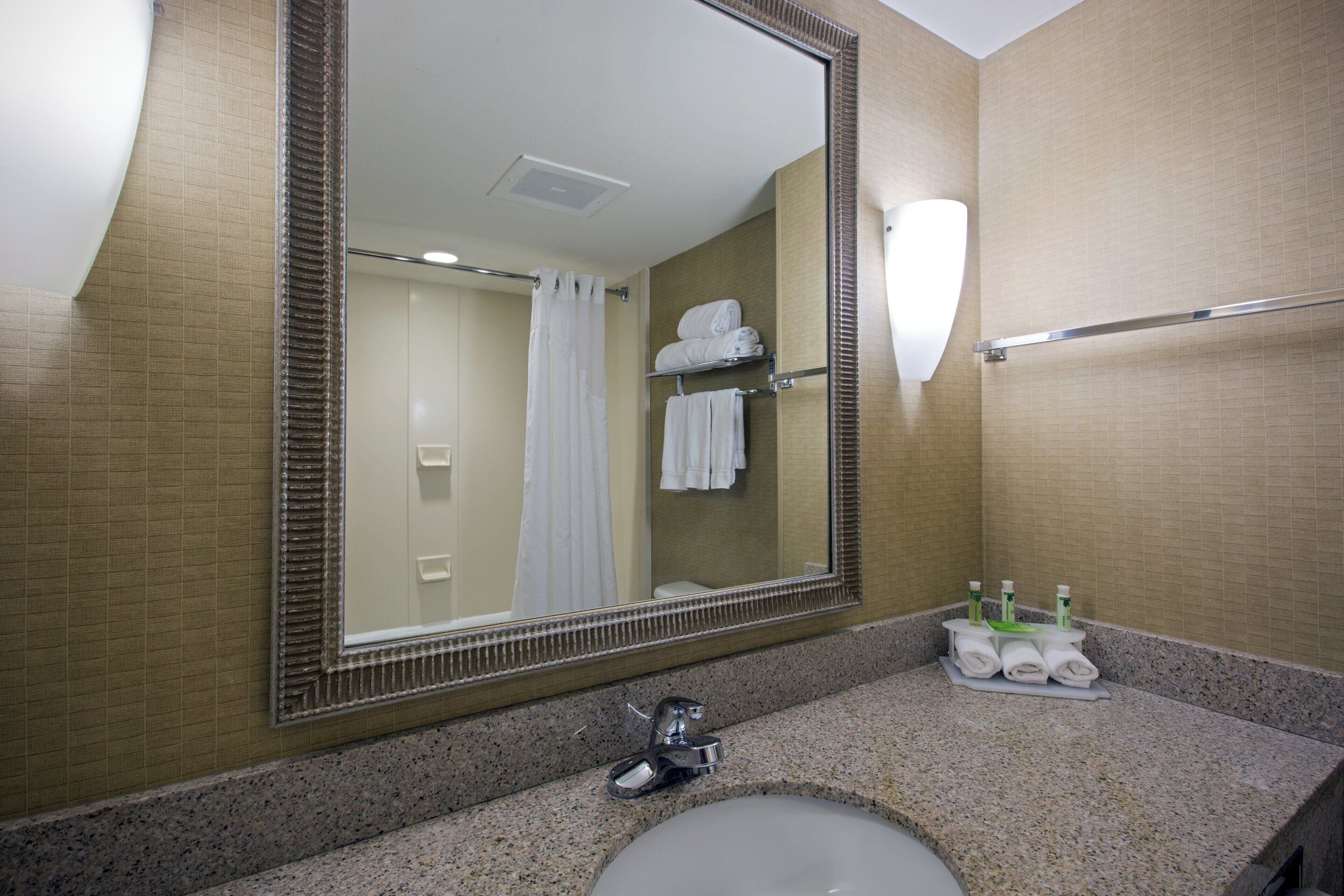 Un baño con un espejo grande, un lavabo, un perchero para toallas y un estante con artículos de aseo.