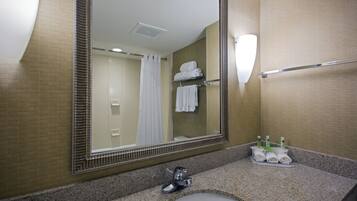 Un baño con un espejo grande, un lavabo, un perchero para toallas y un estante con artículos de aseo.