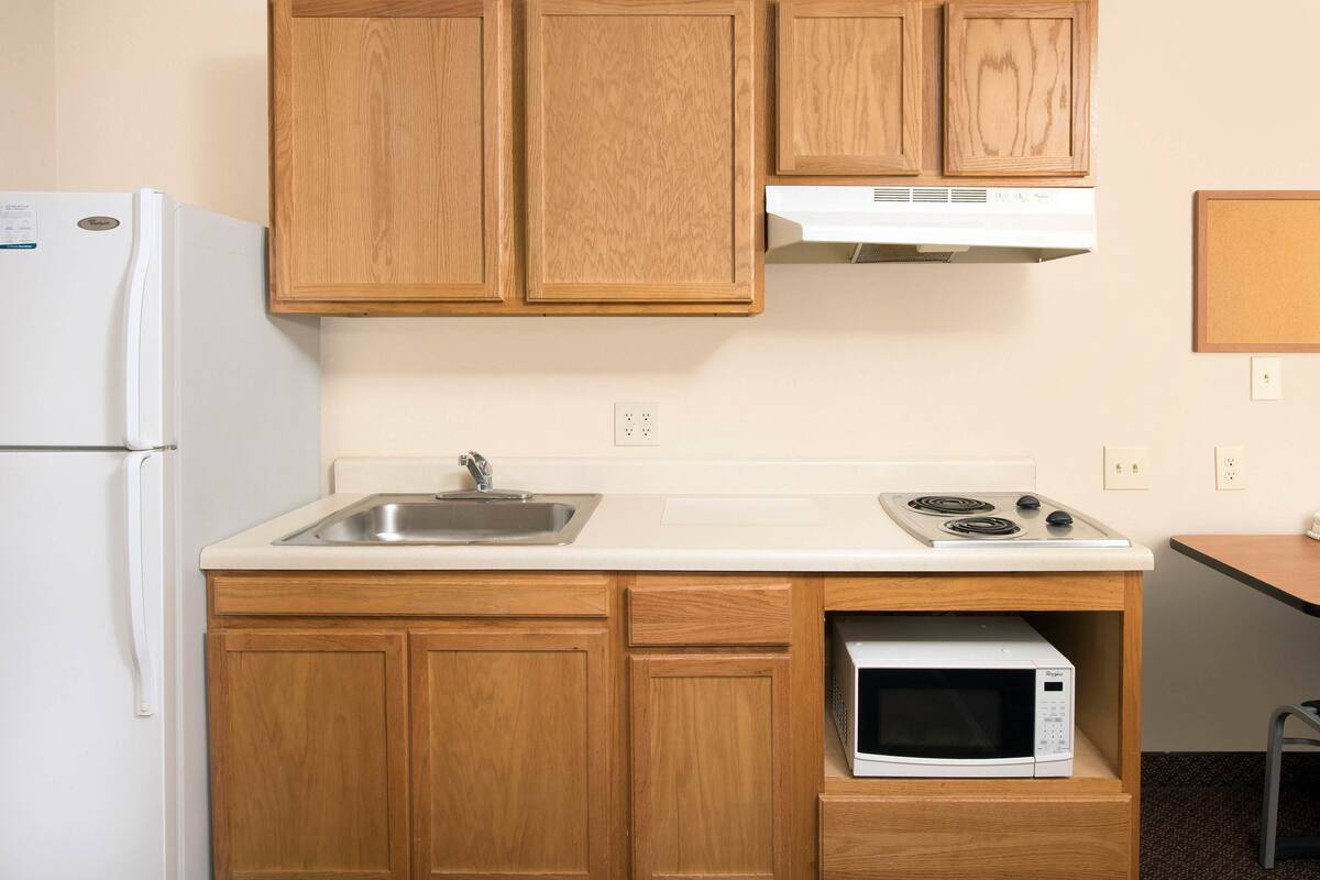 A compact kitchen with wooden cabinets, a white countertop, a built-in microwave, a stove, and a refrigerator.