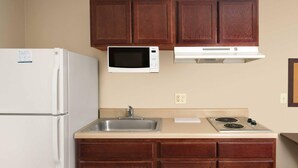 A kitchen with a refrigerator, microwave, sink, stove, and wooden cabinets. - WoodSpring Suites Kansas City Liberty (Liberty)