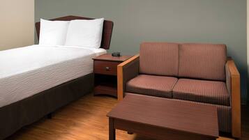 Un dormitorio con cama, mesita de noche y un sofá marrón con su reposapiés a juego.
