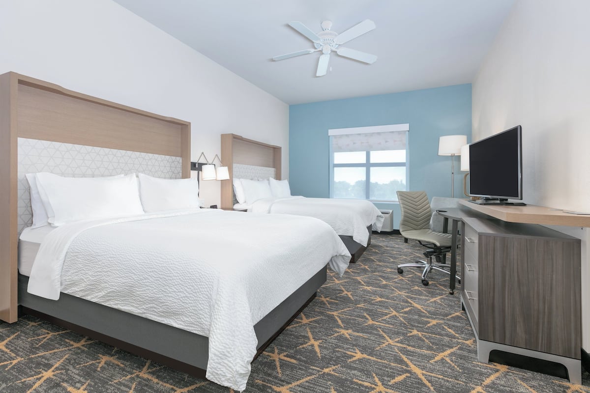 A hotel room with two beds, a desk, a TV, and a ceiling fan.