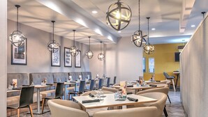 Un restaurant moderne doté de nombreuses tables et chaises, de luminaires sphériques suspendus et d’œuvres d’art encadrées accrochées aux murs.
