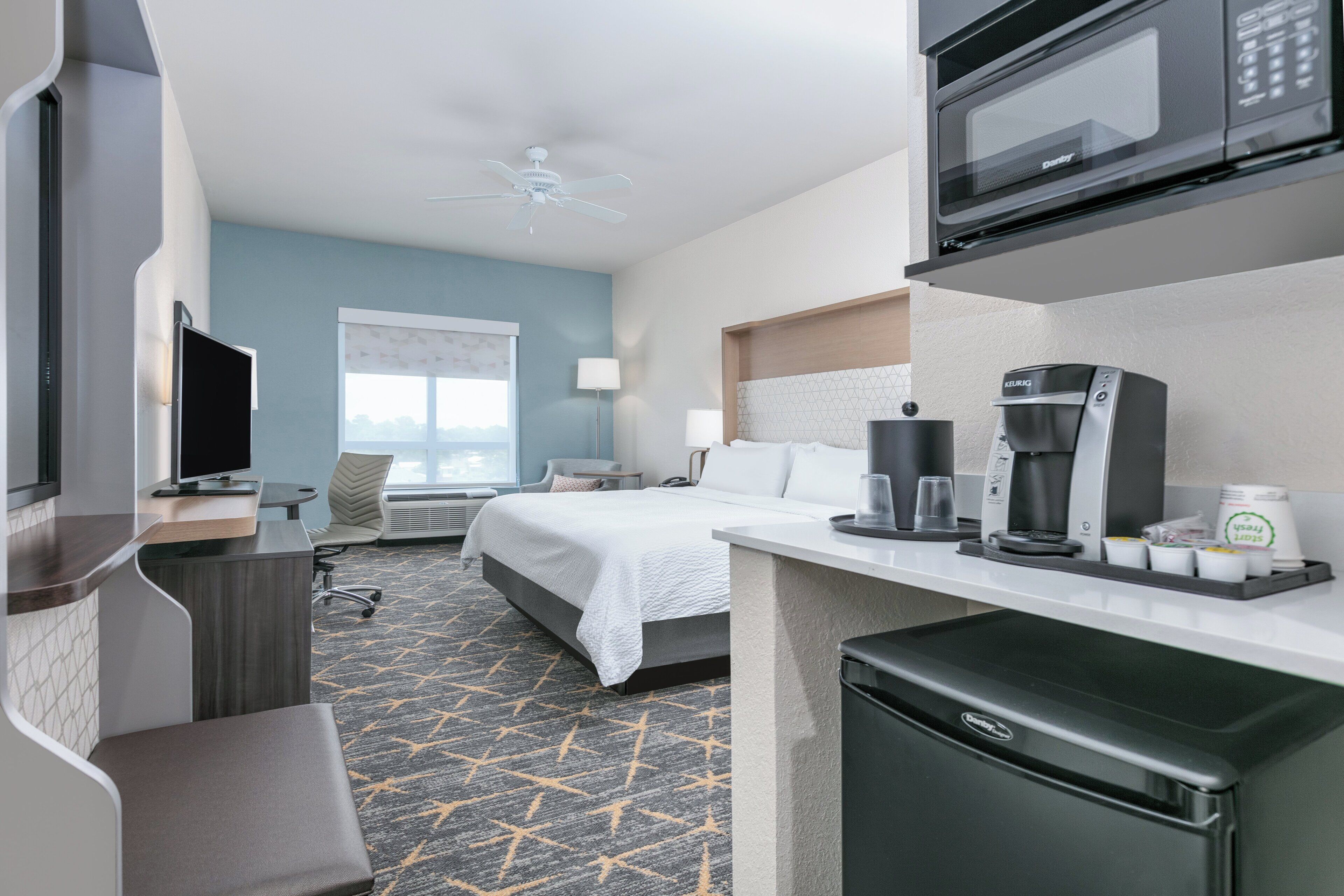 A hotel room with a bed, desk, microwave, coffee maker, and a television.