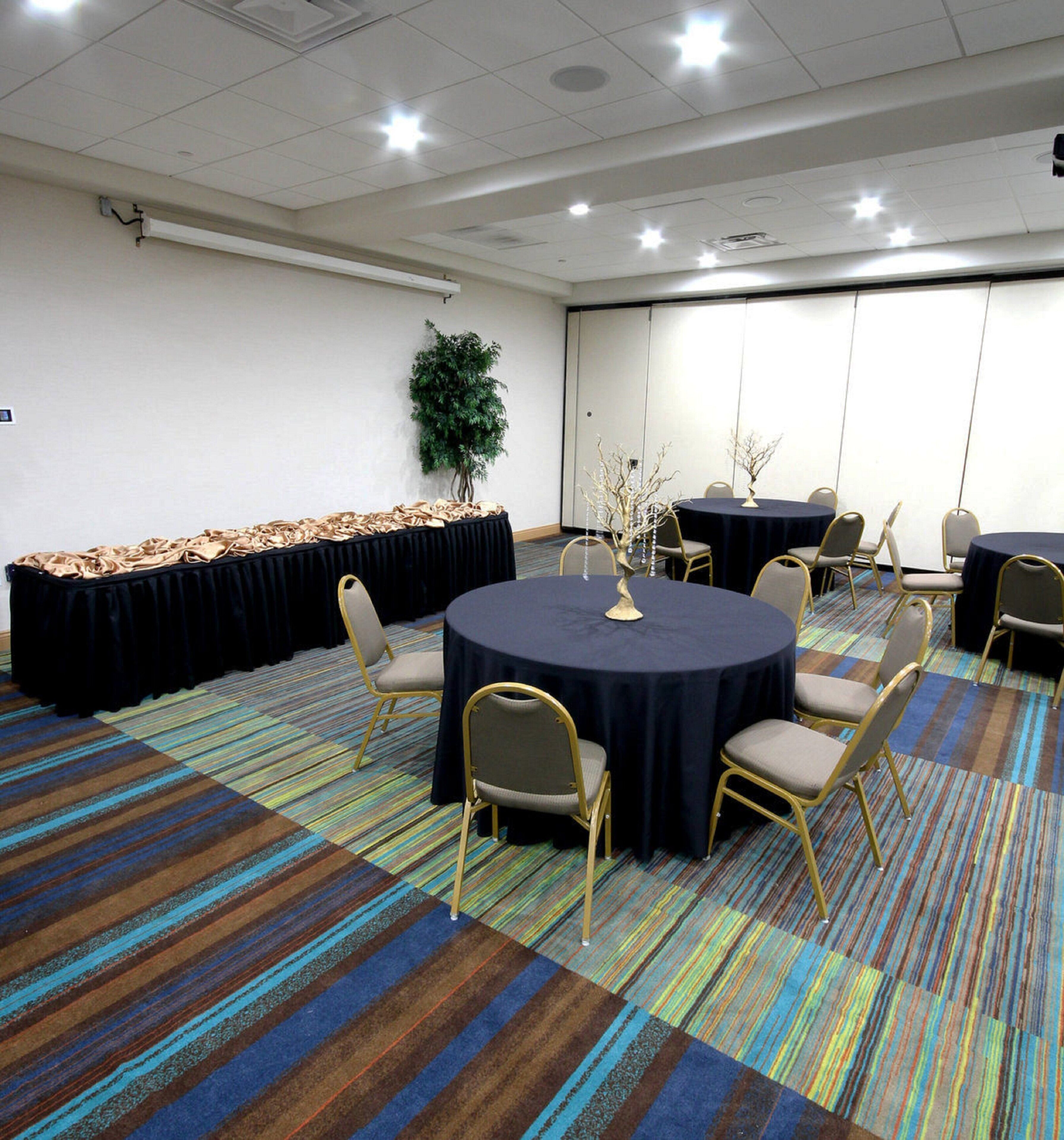 A conference room with a round table, chairs, a projector screen, and a carpeted floor.