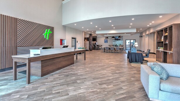 Un espace d’accueil moderne comprenant un comptoir d’accueil en bois, un coin salon avec un canapé et des fauteuils, et un espace repas avec des tables et des chaises.