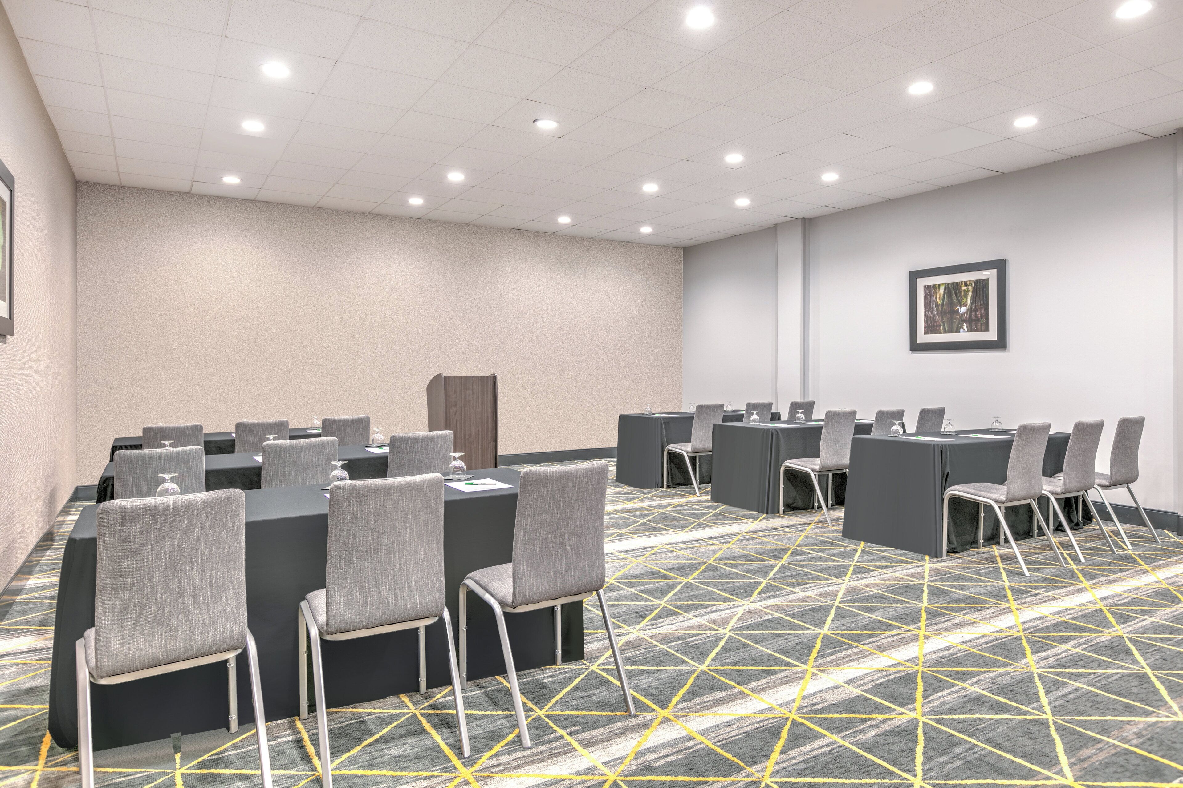 A conference room with tables and chairs, a patterned carpet, and a framed picture on the wall.