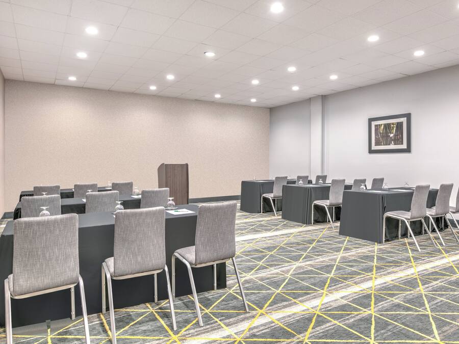 A conference room with tables and chairs, a patterned carpet, and a framed picture on the wall.