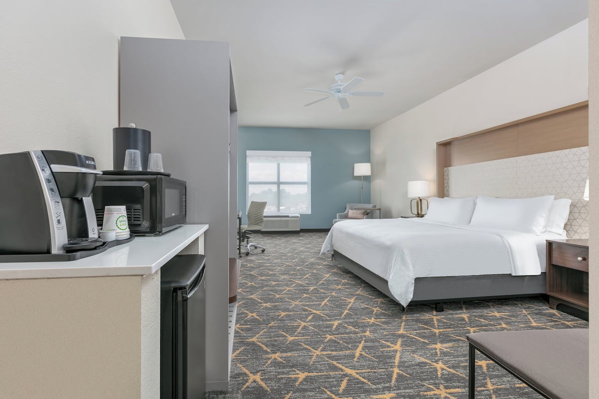 A hotel room with a bed, bedside table, lamp, and a coffee machine.