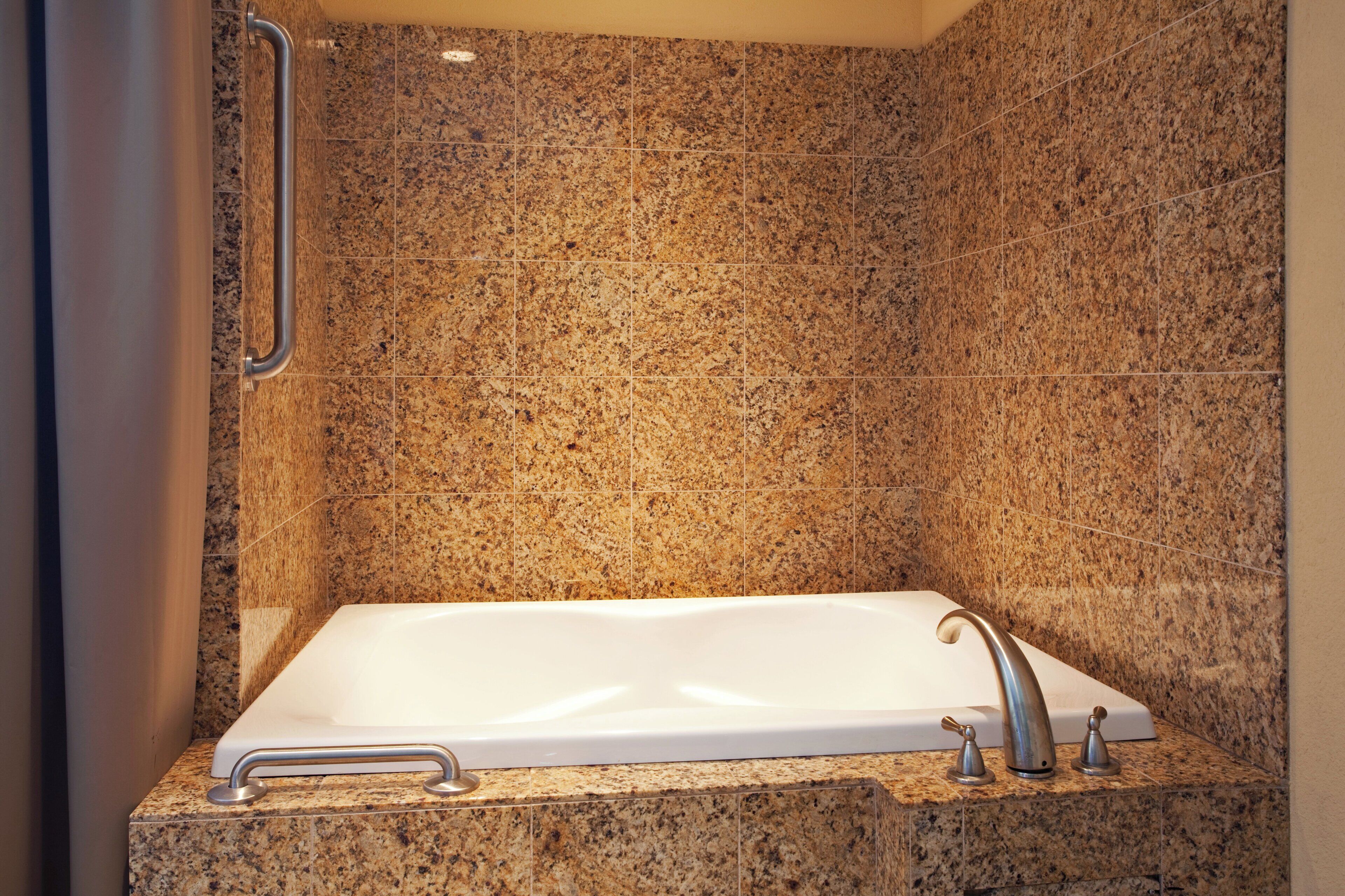 A bathroom with a rectangular bathtub, a handheld showerhead, and a grab bar on the wall.