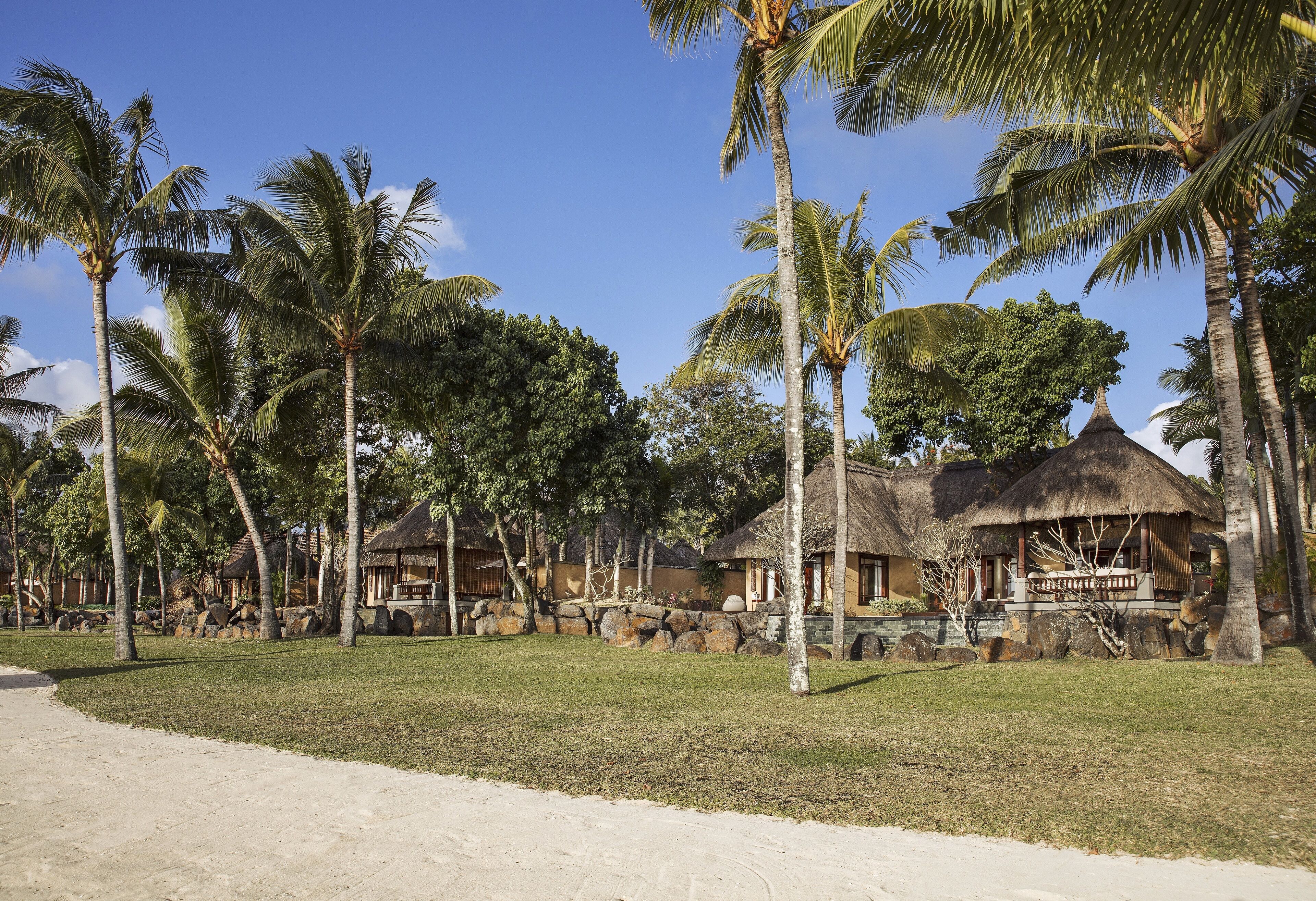 Ein tropisches Resort mit strohgedeckten Hütten, Palmen und blauem Himmel.