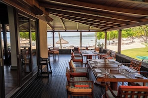 An outdoor dining area with wooden tables and chairs, overlooking a beach and the sea. - Shanti Maurice Resort & Spa (Chemin Grenier)