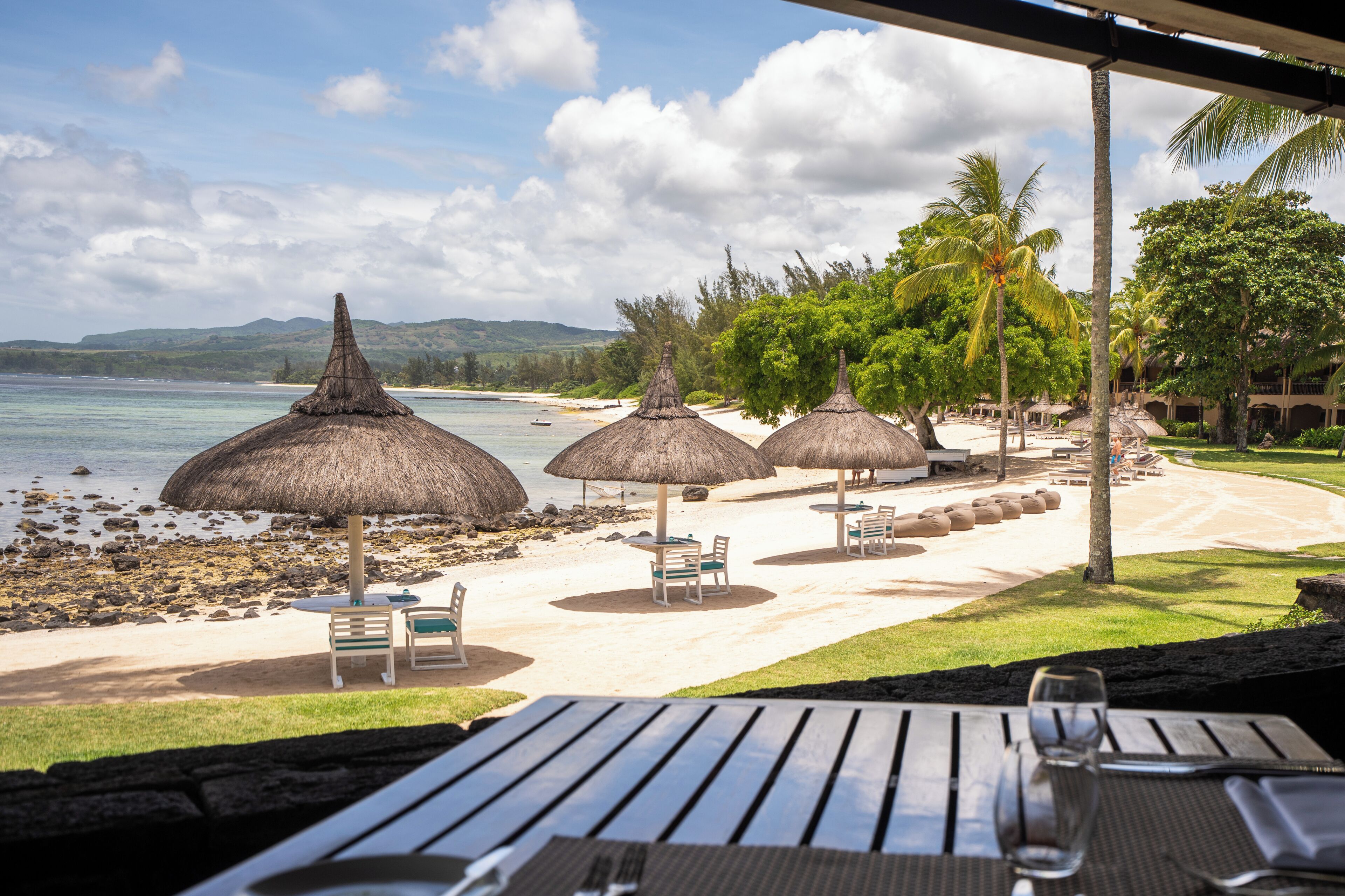 A beachside resort with thatched umbrellas, lounge chairs, and a view of the ocean.