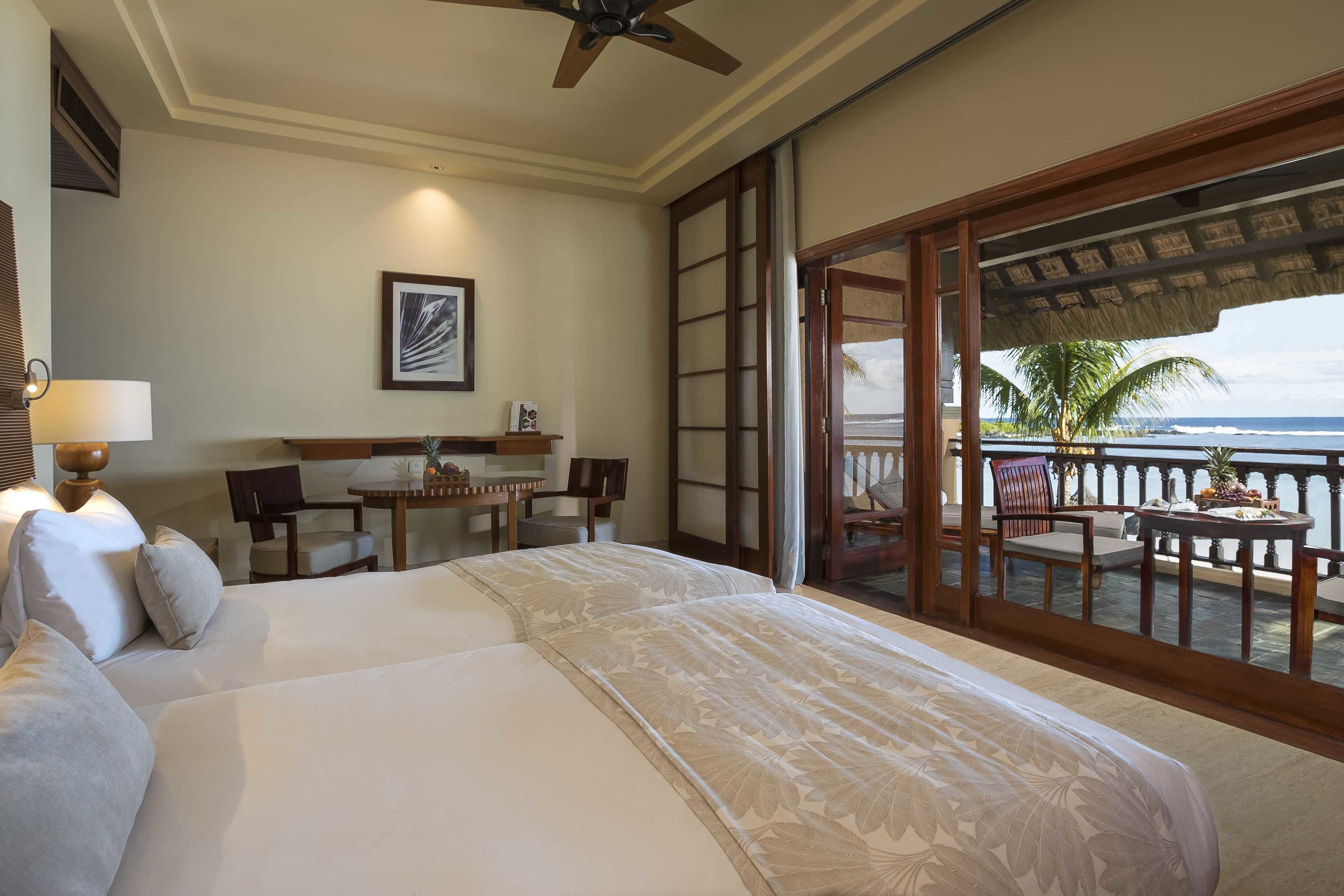 Habitación de hotel con una cama grande, un escritorio y un balcón con vista al océano.