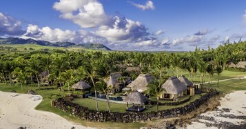 Un resort con cabañas de techo de paja, una piscina y una playa.