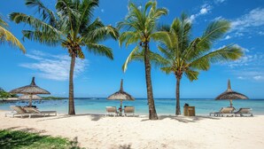 A beach with palm trees, thatched umbrellas, and lounge chairs. - Shanti Maurice Resort & Spa (Chemin Grenier)