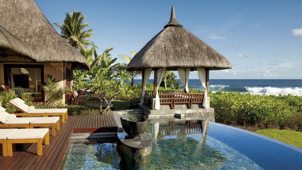 A poolside area with lounge chairs, a thatched-roof gazebo, and a view of the ocean. - Shanti Maurice Resort & Spa (Chemin Grenier)