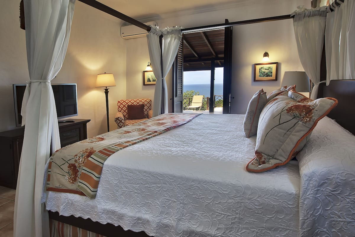 Ein Schlafzimmer mit Bett, Fernseher, Stuhl und einem Balkon mit Blick.