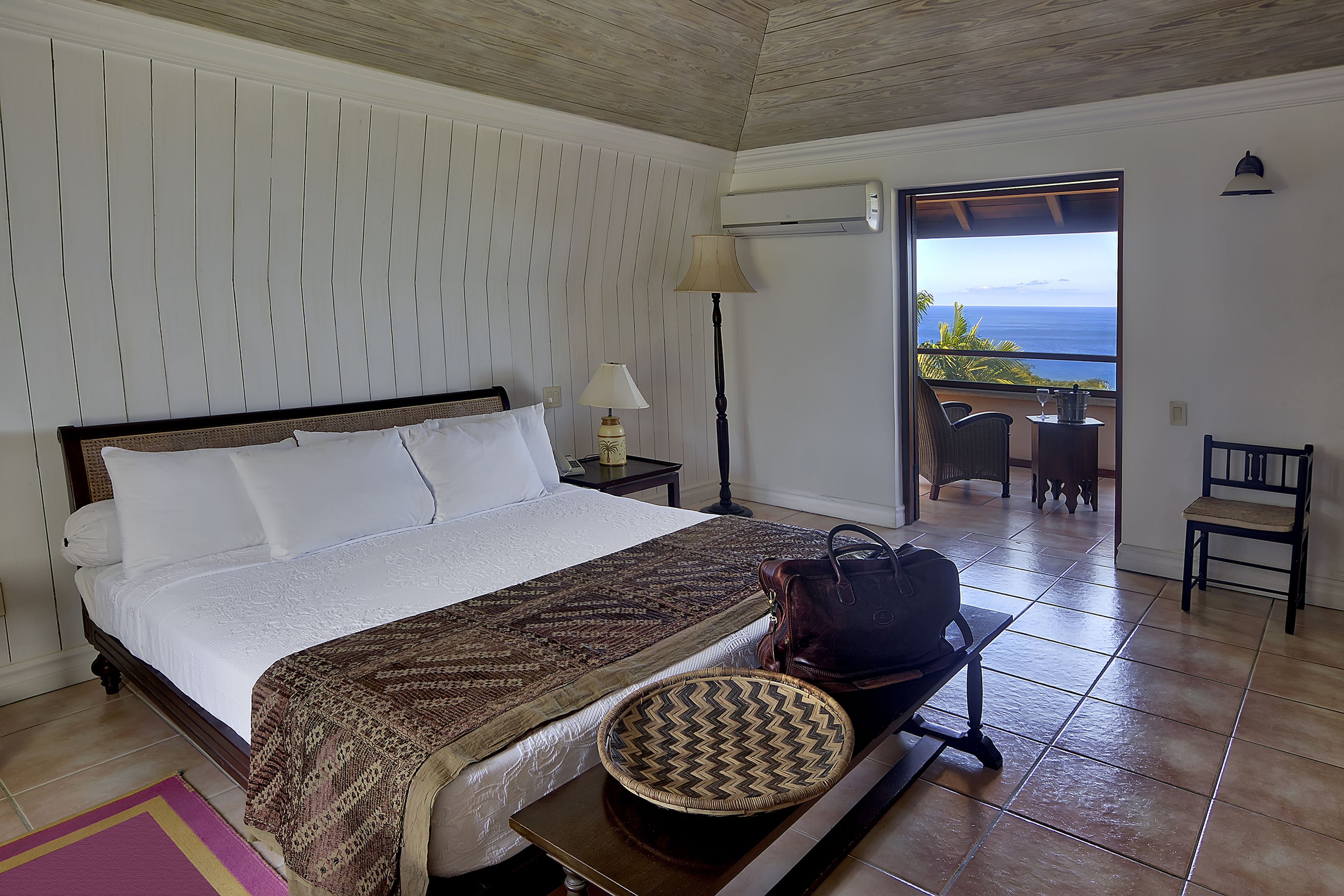 A hotel room with a bed, a lamp, a chair, a table, and a view of the ocean.
