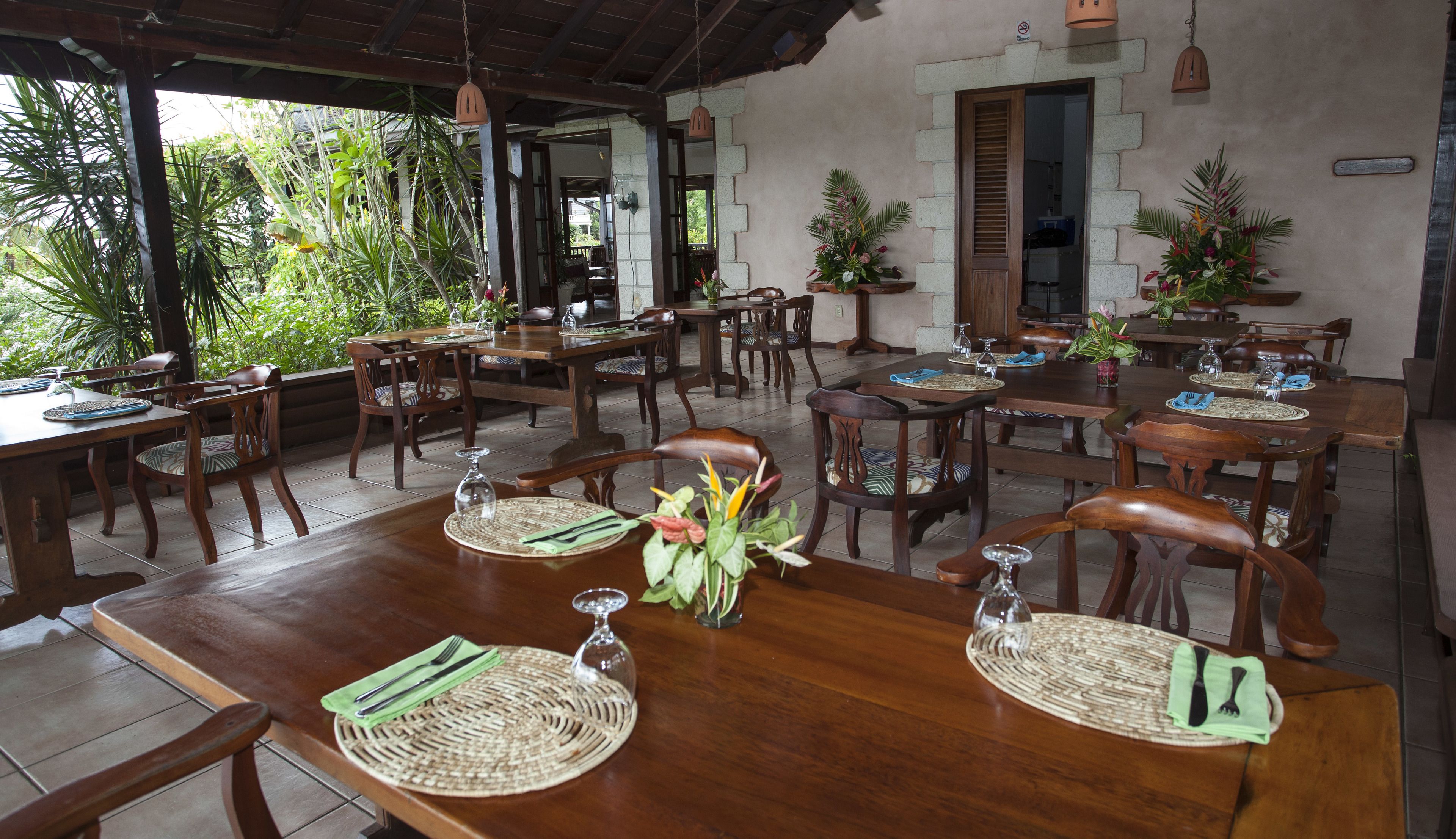 A restaurant with wooden tables and chairs, surrounded by greenery.