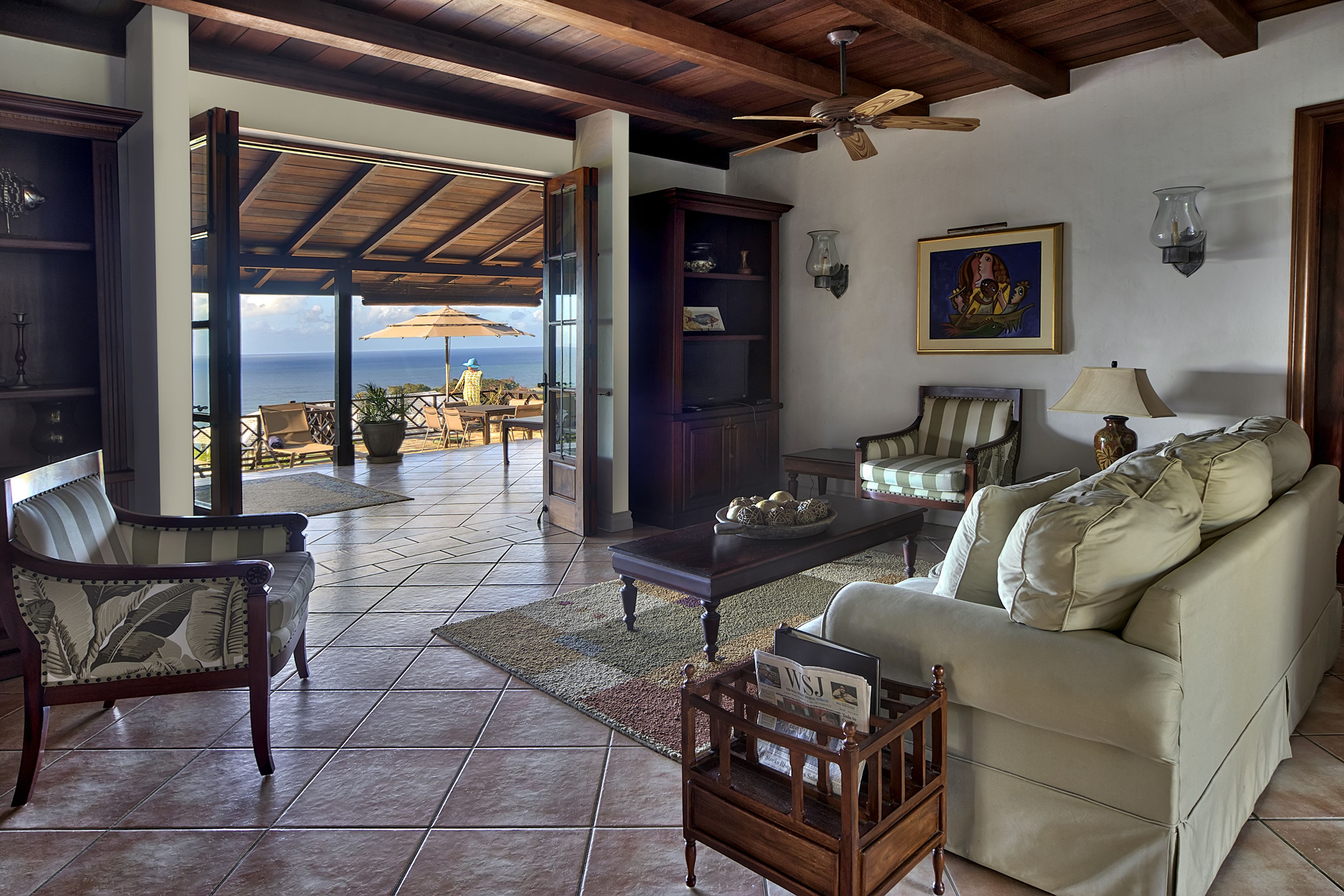 A spacious living area with a view of the ocean, a ceiling fan, and a wooden coffee table.