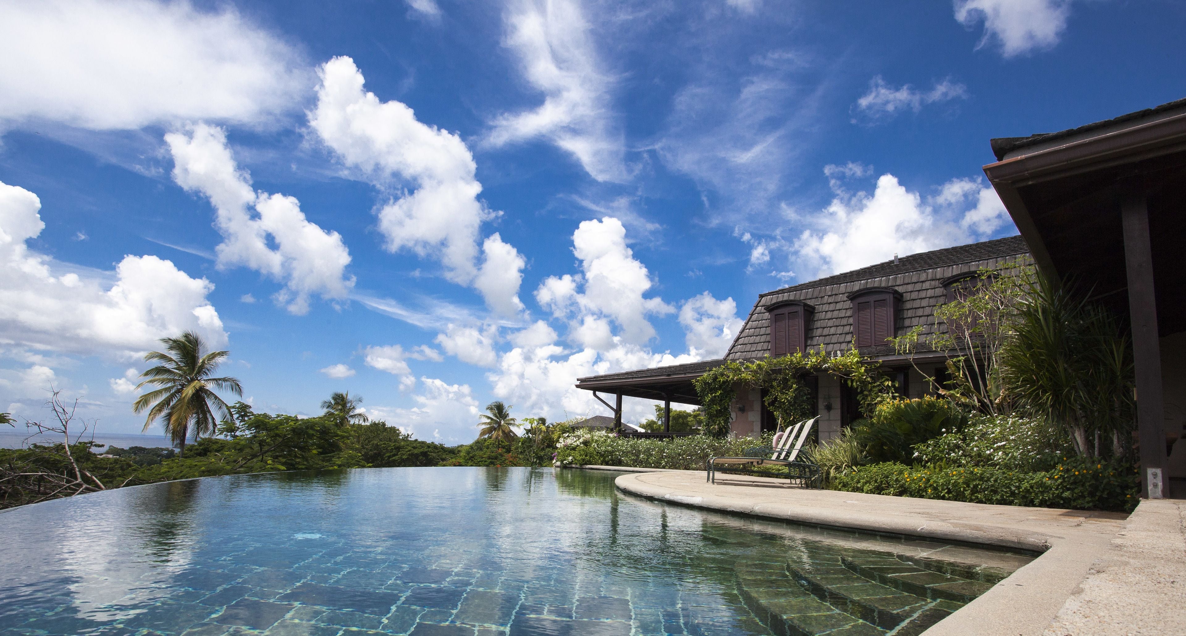 A pool with clear water, a palm tree, and a building with a sloped roof.