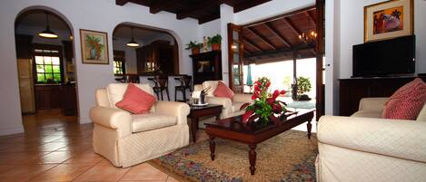 A spacious living room with two beige sofas, a wooden coffee table, and a large window offering a view of the outdoors.