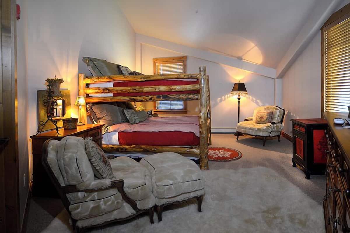 Un dormitorio acogedor con una litera, una silla, una lámpara y un aparador.