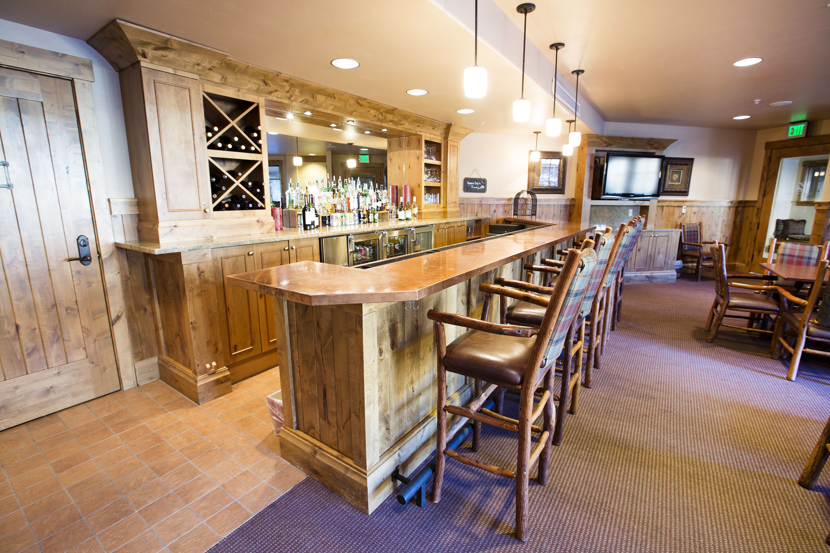 A bar area with wooden bar stools, a counter with bottles, and a television screen.