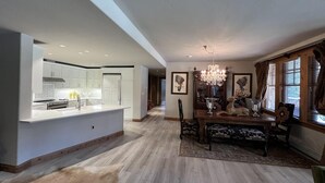 Una cocina amplia con armarios blancos y una isla central, un comedor con mesa y sillas de madera, y una araña.
