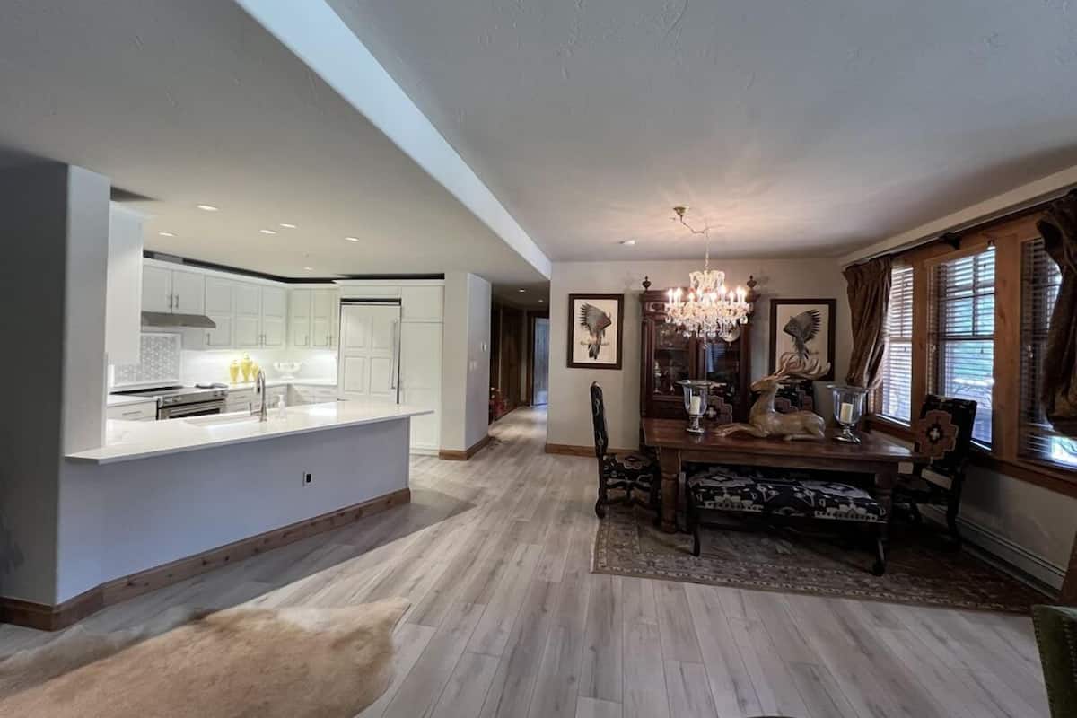 Una cocina amplia con armarios blancos y una isla central, un comedor con mesa y sillas de madera, y una araña.