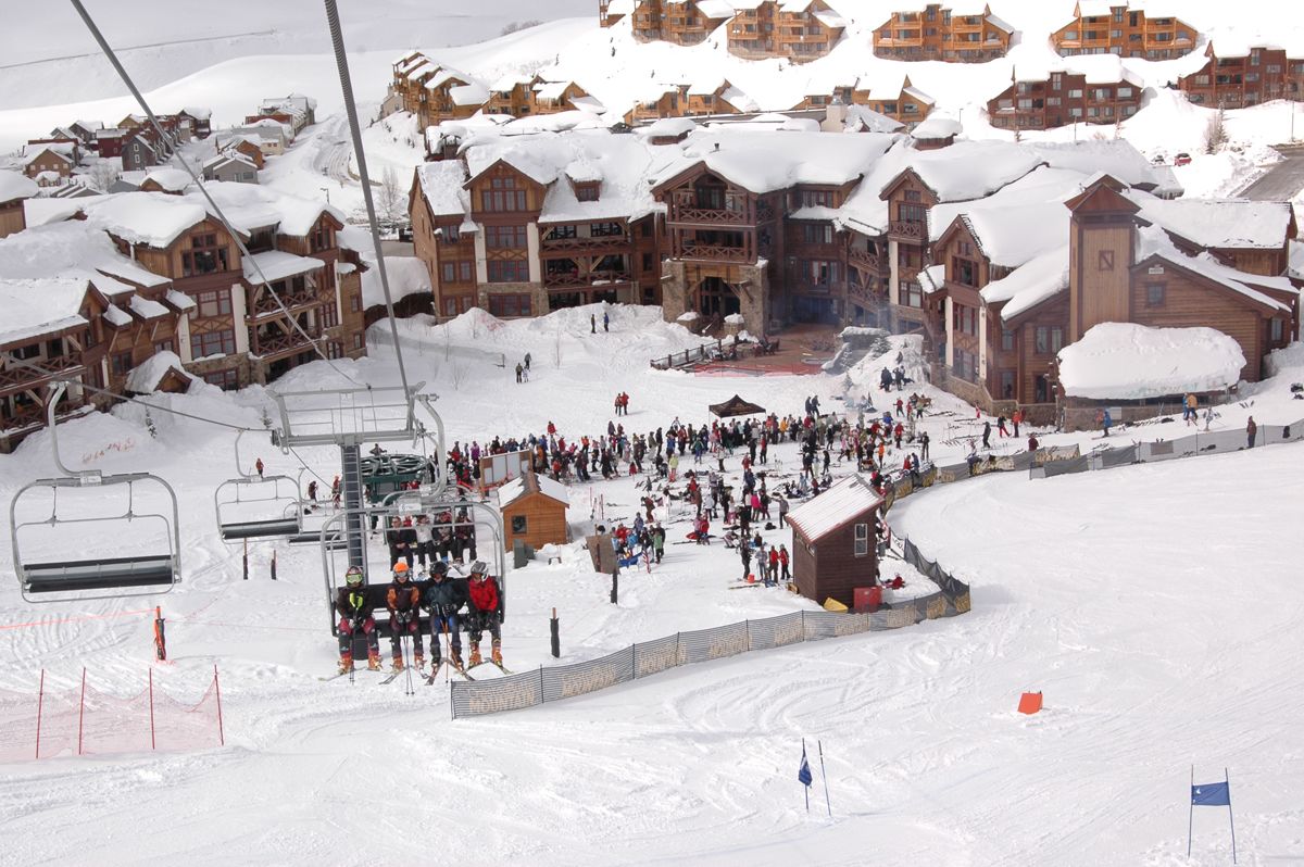 Een ski-resort met houten gebouwen, skiliften en veel mensen.