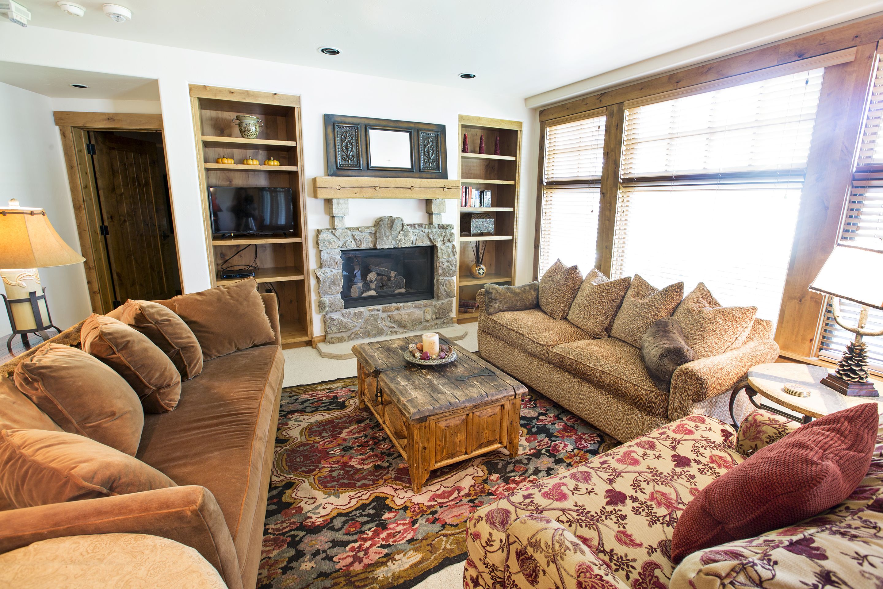 A cozy living room with a stone fireplace, wooden shelves, and a large window.