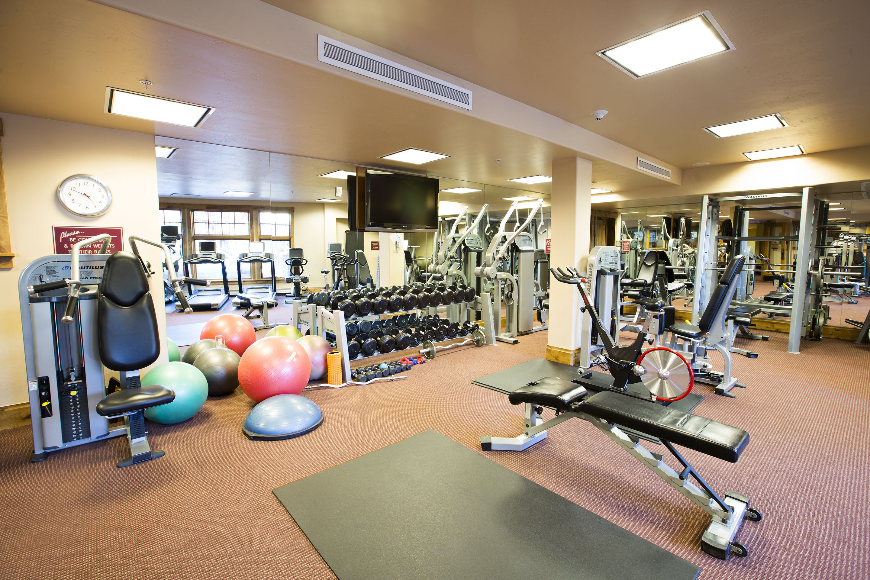 Ein Fitnessstudio mit unterschiedlichen Trainingsgeräten, darunter Laufbänder, Kurzhanteln und Gymnastikbälle.