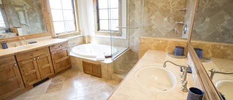 A modern bathroom with a large bathtub, two sinks, and a walk-in shower.