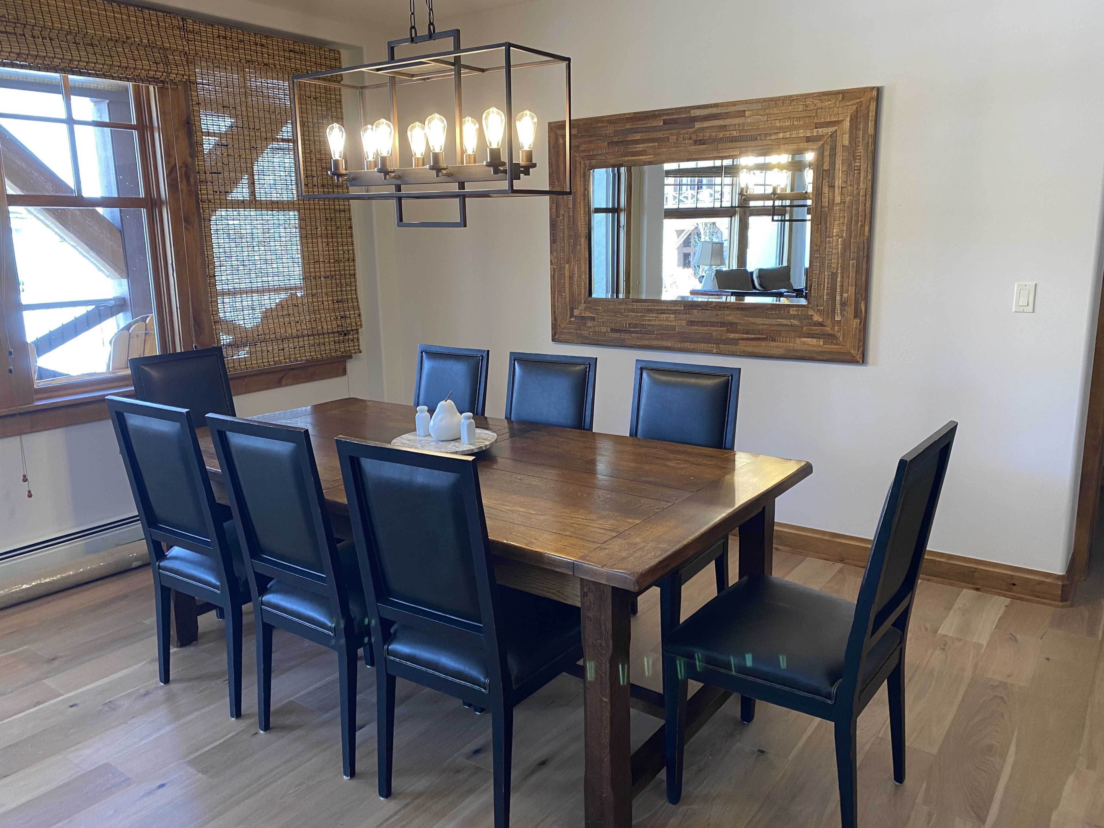 A dining area with a wooden table, six chairs, a chandelier, and a large mirror.