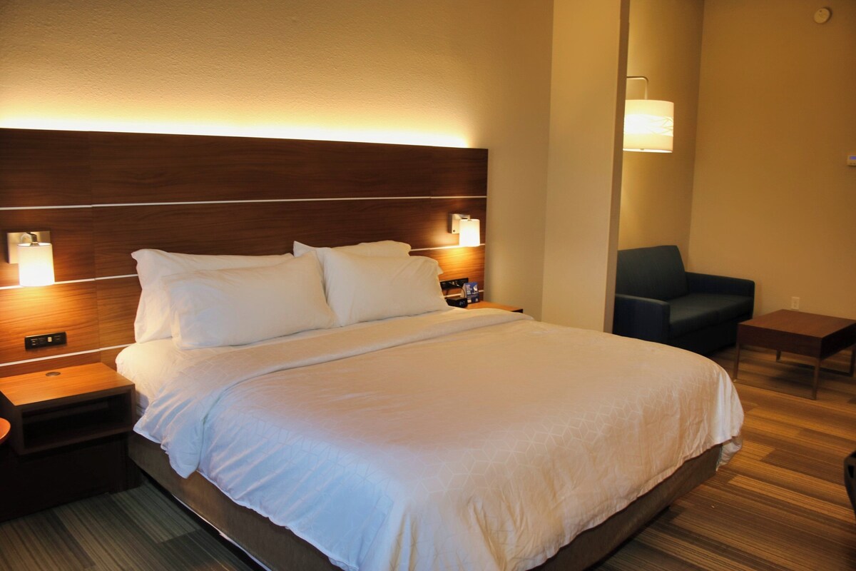 Una habitación de hotel con una cama grande, lámparas de noche, una mesita y una silla.