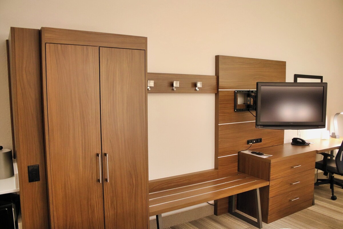 Un dormitorio moderno con un armario de madera, un escritorio con televisor de pantalla plana y una silla.